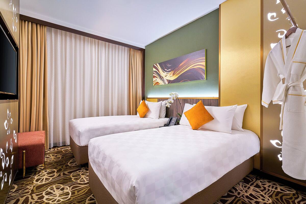 A hotel room with two beds, a TV, a painting, and a robe rack.