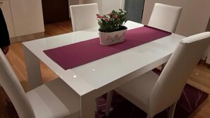 A white dining table with a purple placemat, surrounded by white chairs. A potted plant with pink flowers is placed on the table. - Casa Garofoli (Frascati)