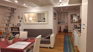 A modern living room with a sofa, a dining table with a red plaid tablecloth, and a kitchen area with a stove and cabinets.
