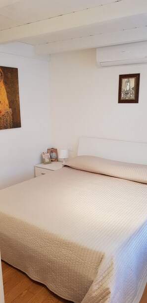 A bedroom with a large bed, a nightstand with a lamp, and a painting on the wall. - Casa Garofoli (Frascati)