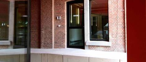 A brick building with a glass entrance, a sign reading "ROOMS", and a red awning.