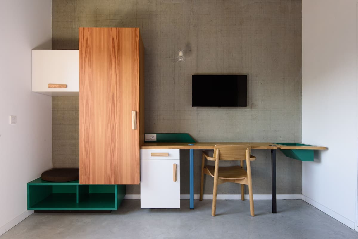 Ein kleines Zimmer mit Schreibtisch, Stuhl und Kleiderschrank.