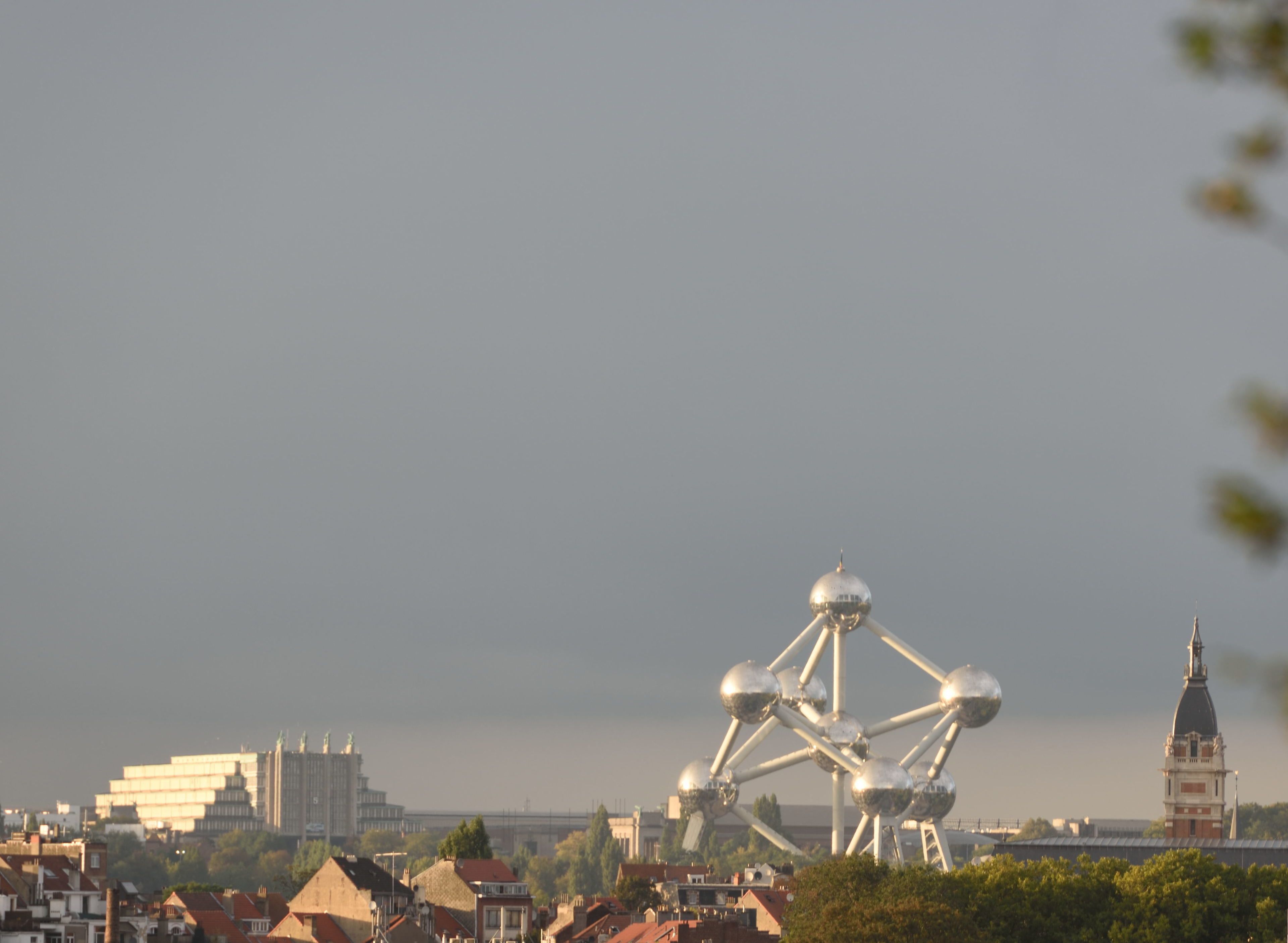 Bybillede med Atomium i centrum, omgivet af boligbygninger og et historisk tårn.