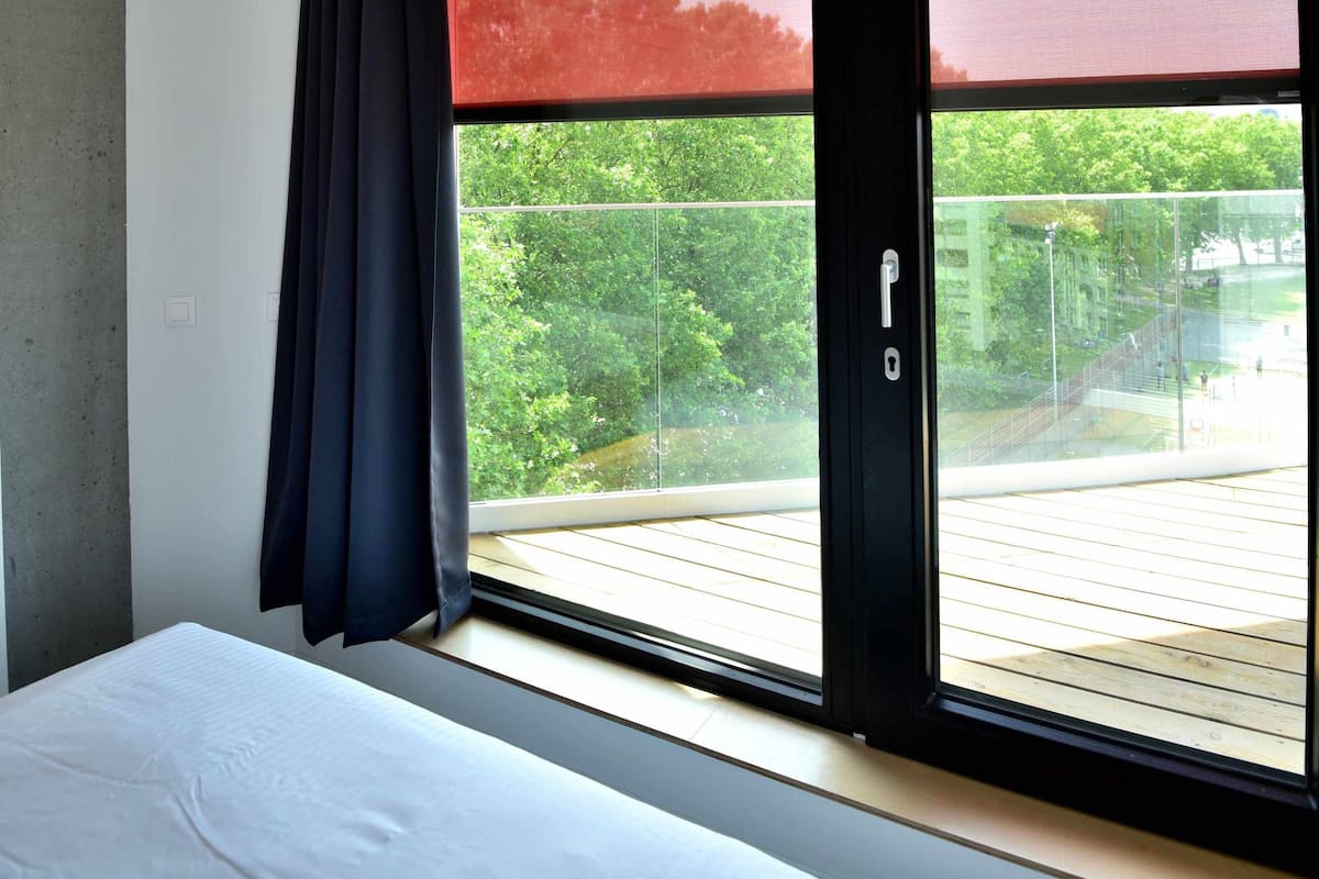 Ein Schlafzimmer mit großem Fenster, einem Bett und Blick auf einen Balkon.