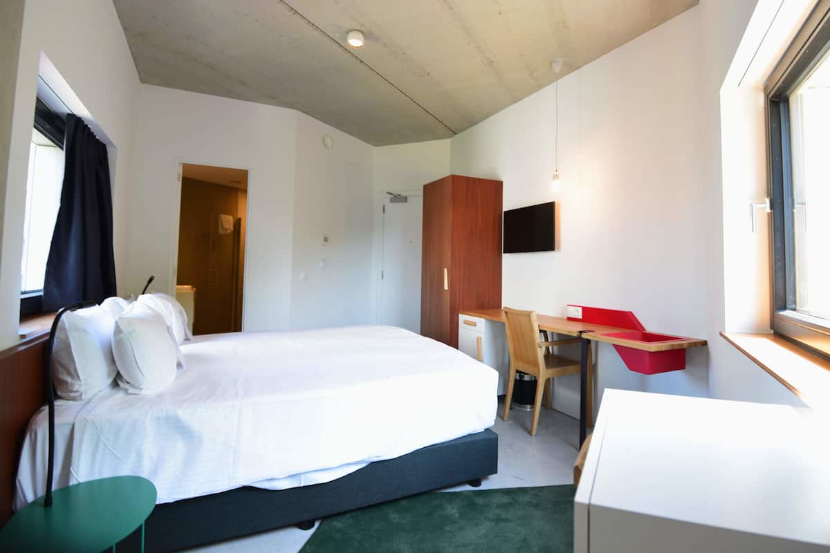 Ein Hotelzimmer mit einem Bett, einem Schreibtisch, einem Sessel, einem Fernseher und einem Fenster.