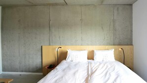 A bedroom with a large bed, a wooden headboard, and a concrete wall. - BELVUE Hotel (Brussels)