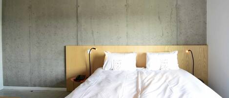 A bedroom with a large bed, a wooden headboard, and a concrete wall.