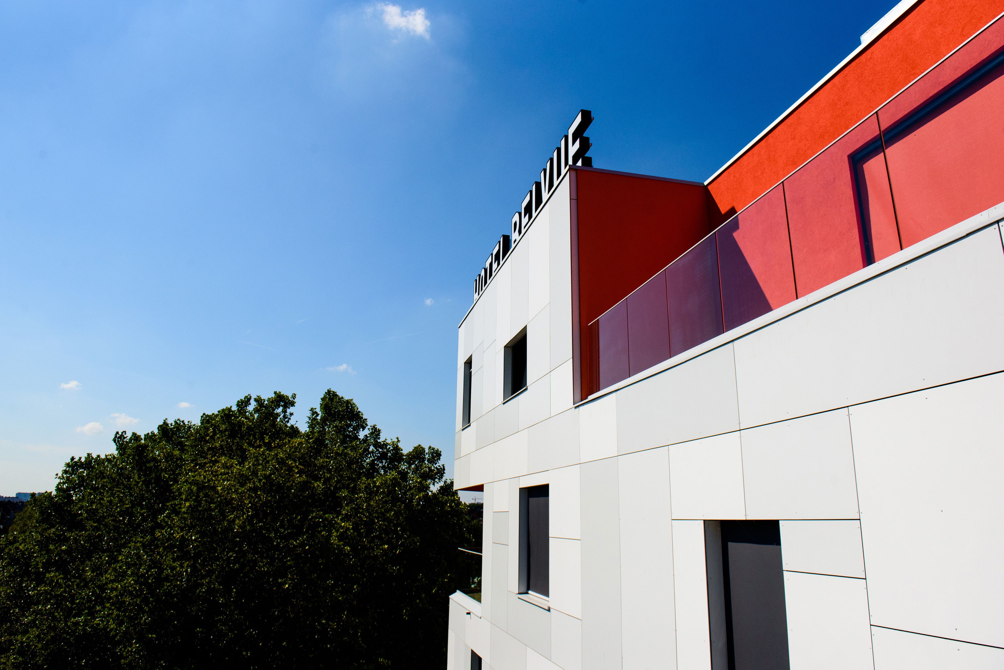 Ein modernes Gebäude mit einer roten und weißen Fassade, großen Fenstern und blauem Himmel im Hintergrund.