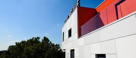 Ein modernes Gebäude mit einer roten und weißen Fassade, großen Fenstern und blauem Himmel im Hintergrund.
