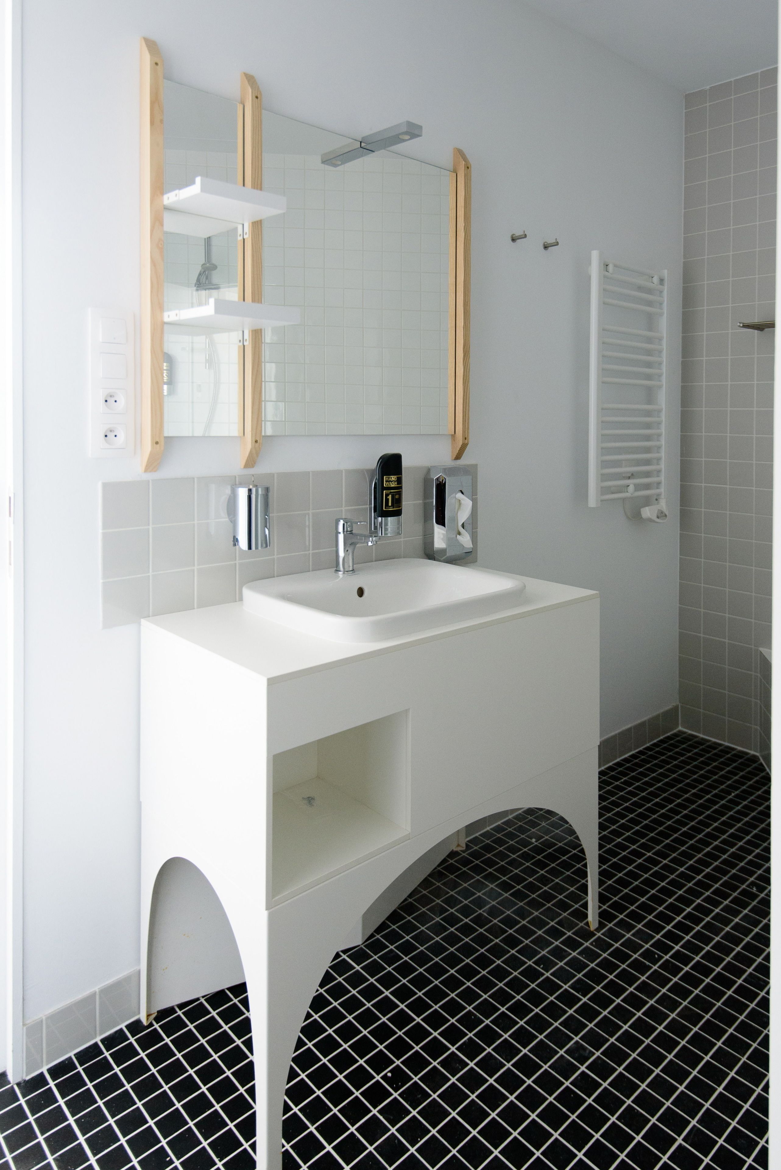 A modern bathroom with a white vanity, a large mirror, and a black and white tiled floor.