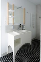 Un baño moderno con un tocador blanco, un espejo grande y un suelo de baldosas blanco y negro.