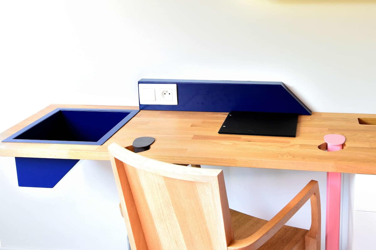 Ein Holztisch mit einer blauen Trennwand, einem schwarzen Laptop und einer rosa Tasse.