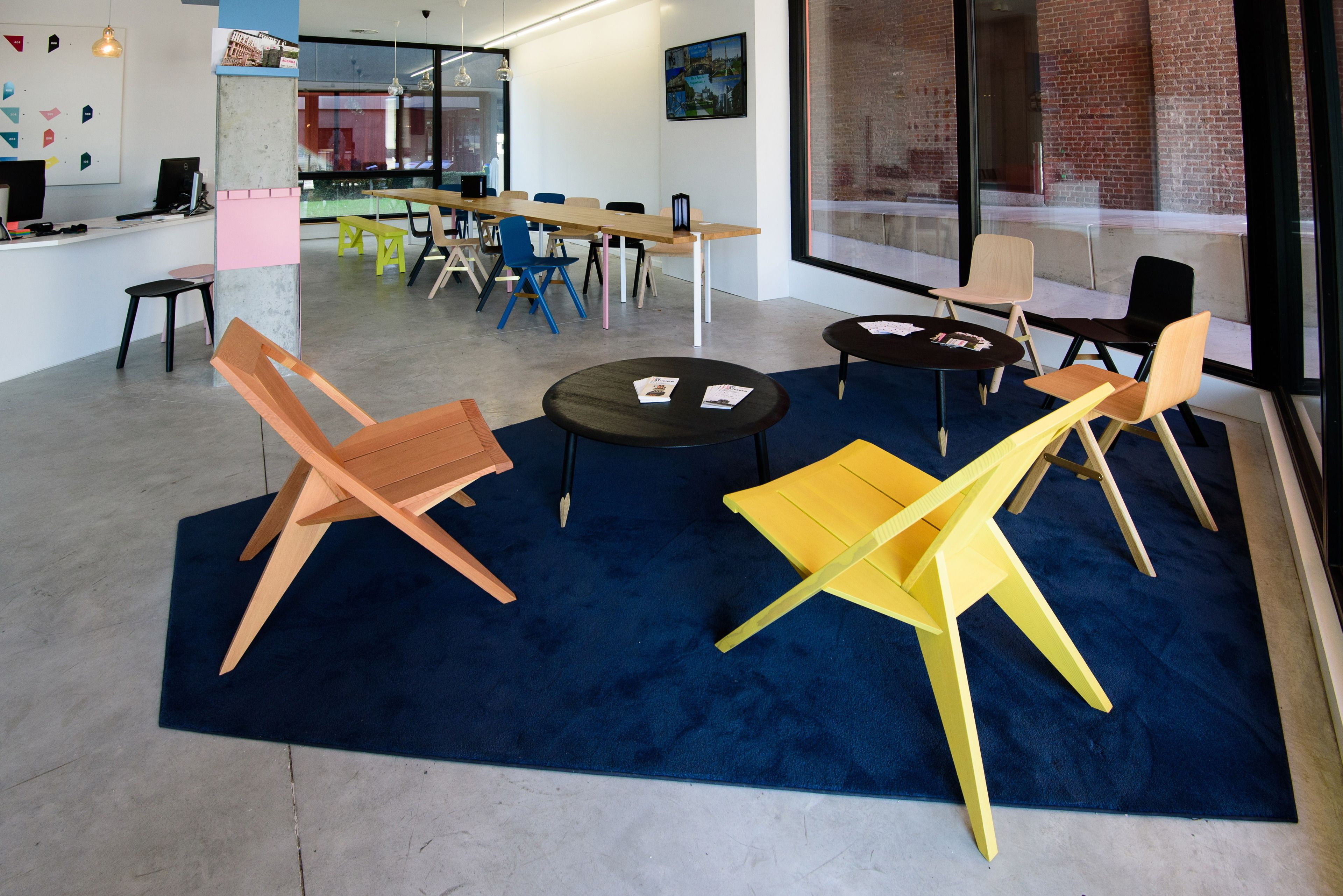 A modern office space with a long table, several chairs, and a blue carpet.