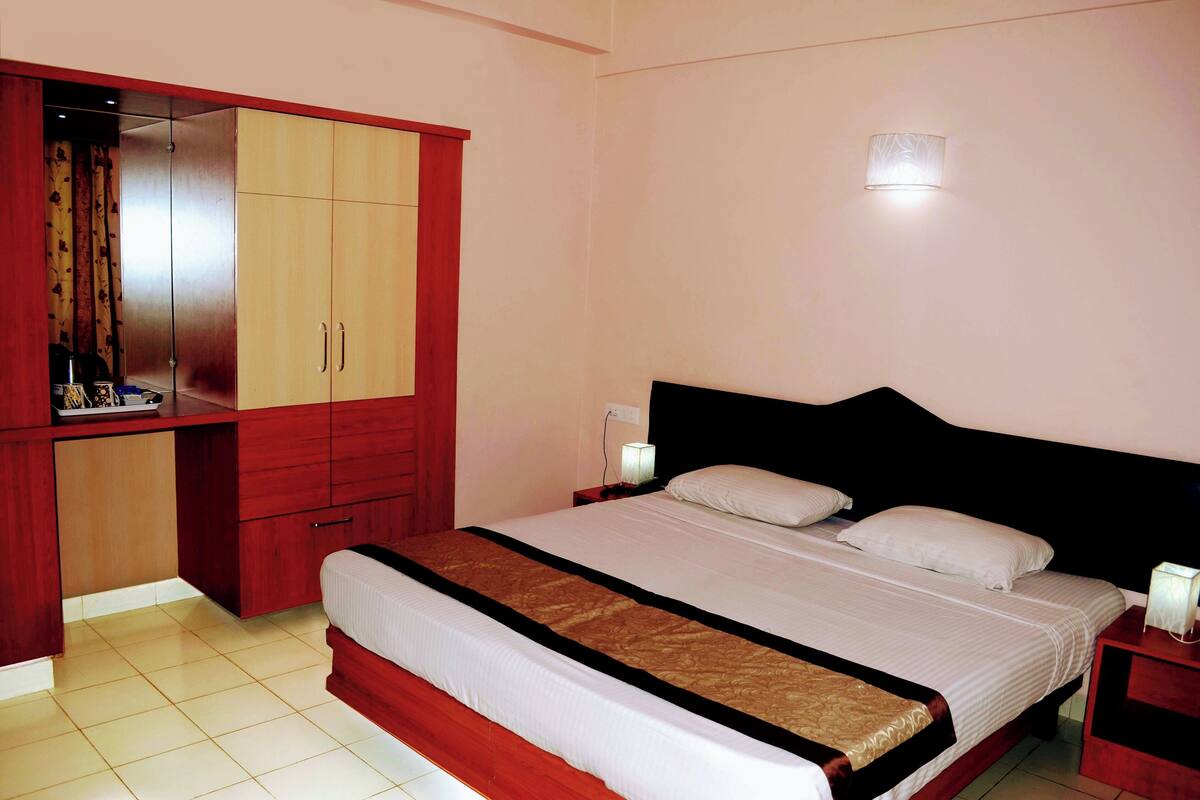 A bedroom with a bed, a wardrobe, a nightstand, and a wall-mounted light fixture.
