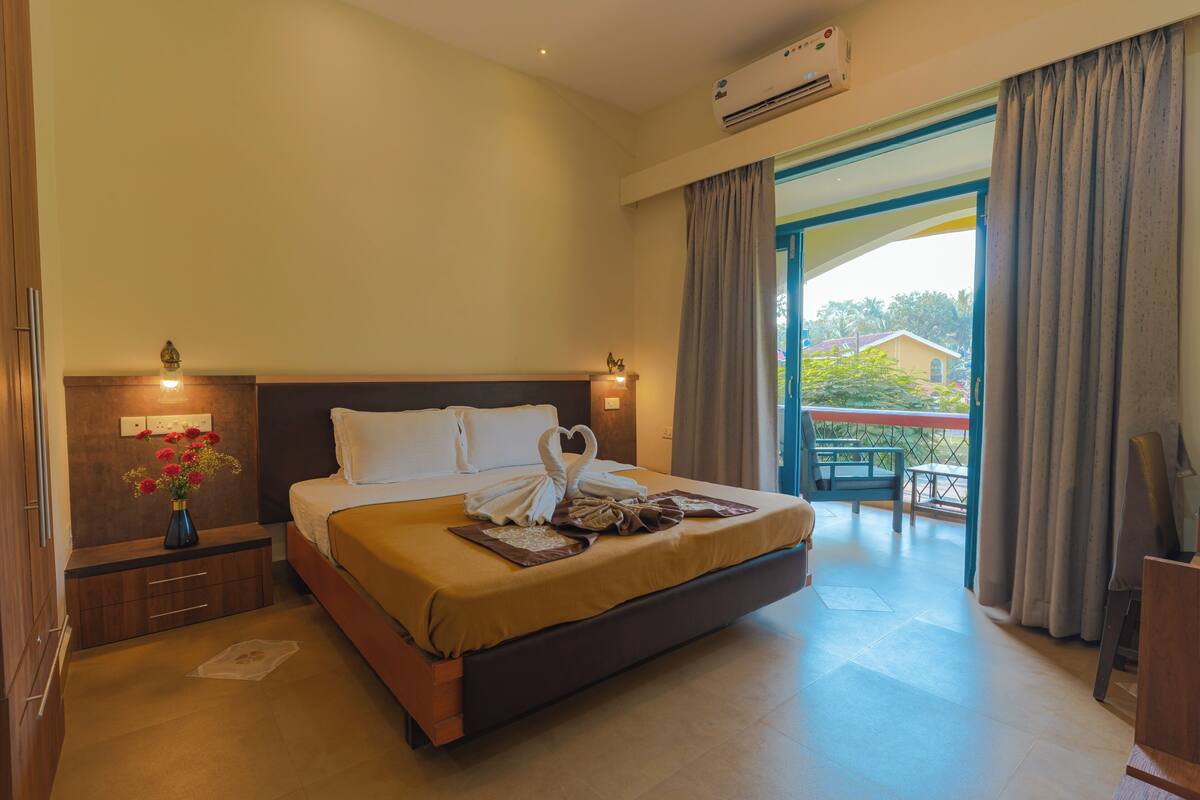 A hotel room with a large bed, a nightstand with a vase of flowers, and a view of the outside balcony.