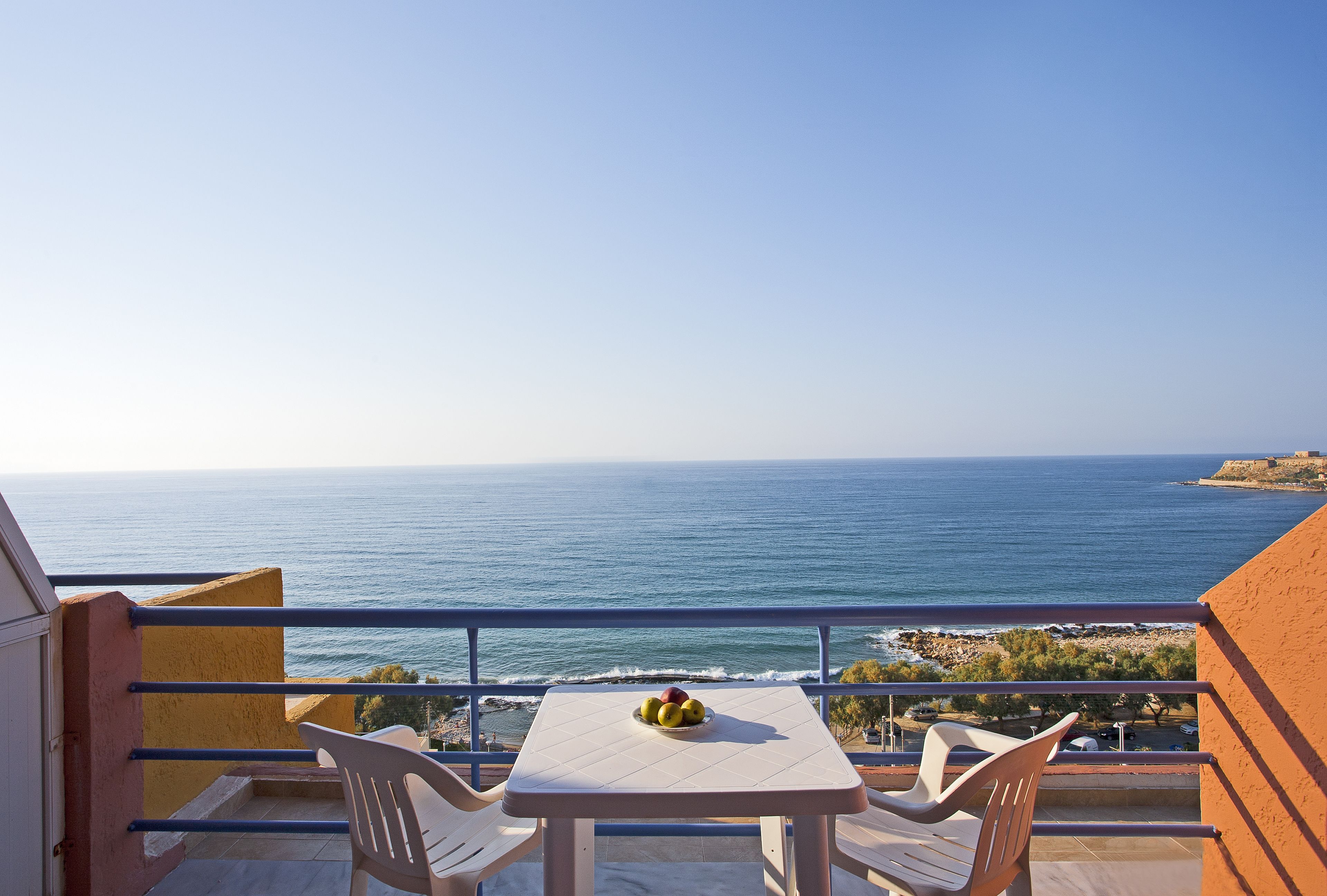 A balcony with a table and chairs overlooking the sea.
