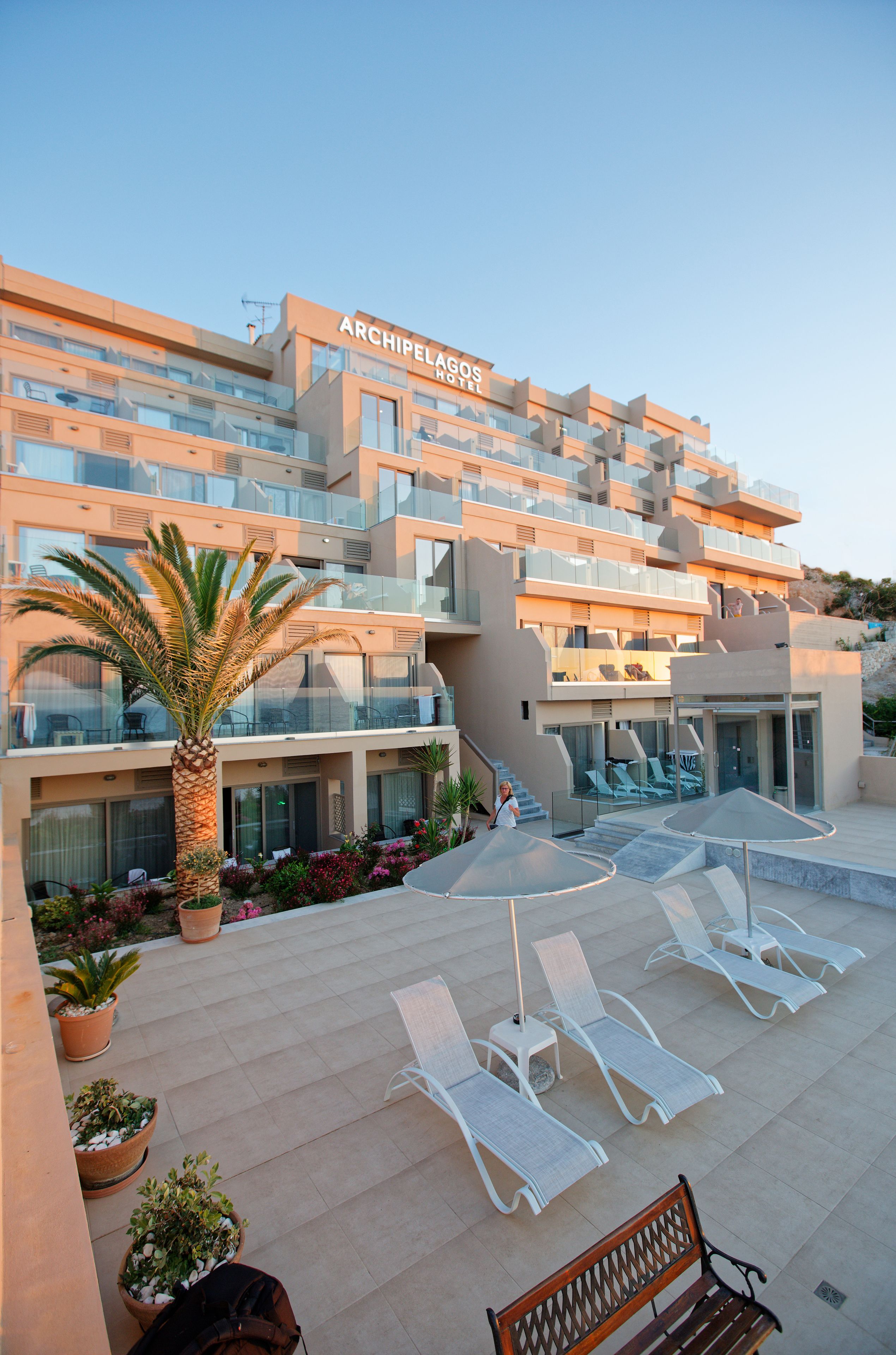 Un hotel moderno con diversi balconi, area salotto esterna e una palma.