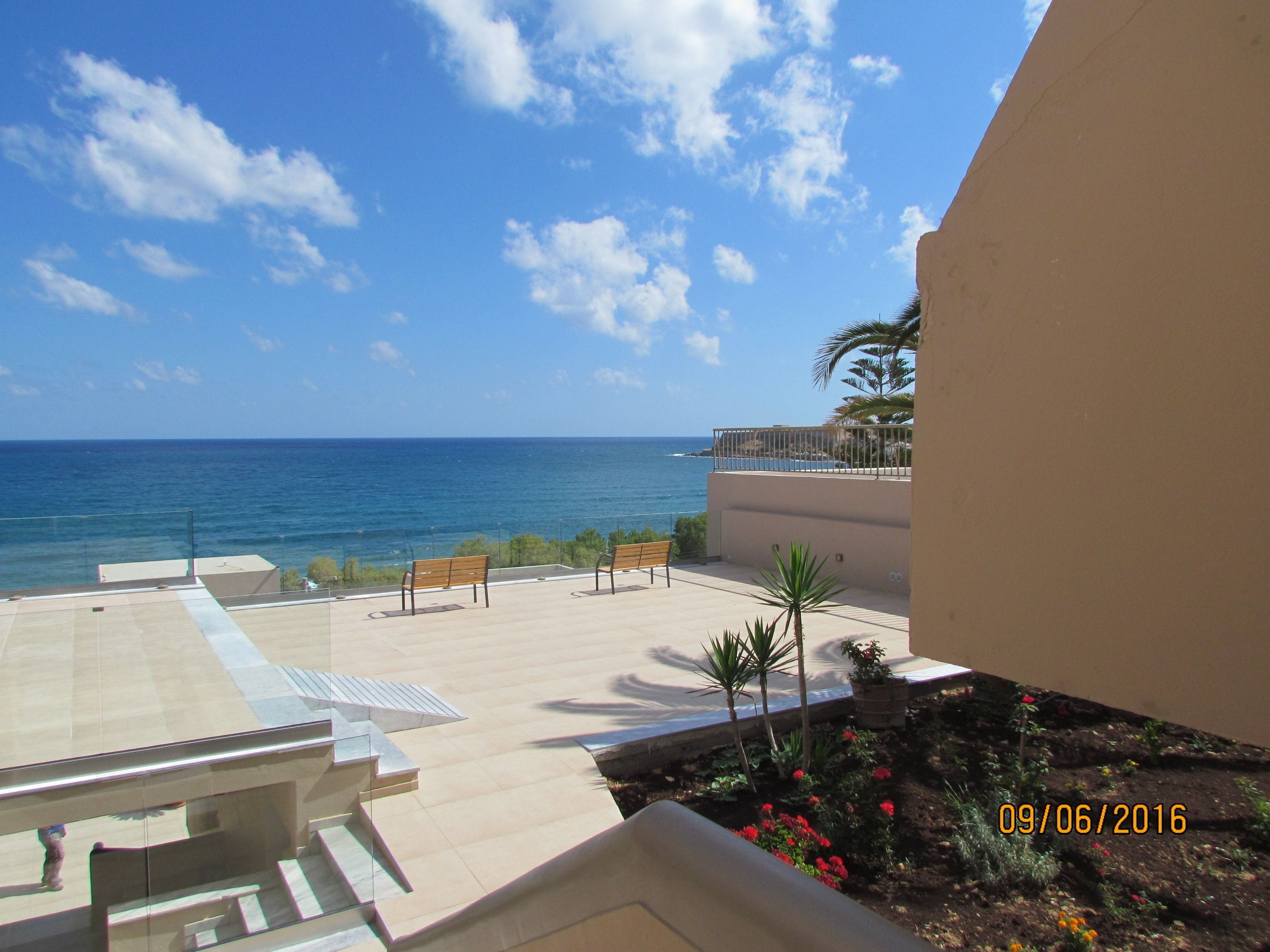 Un balcon avec vue sur la mer, un palmier et un banc.