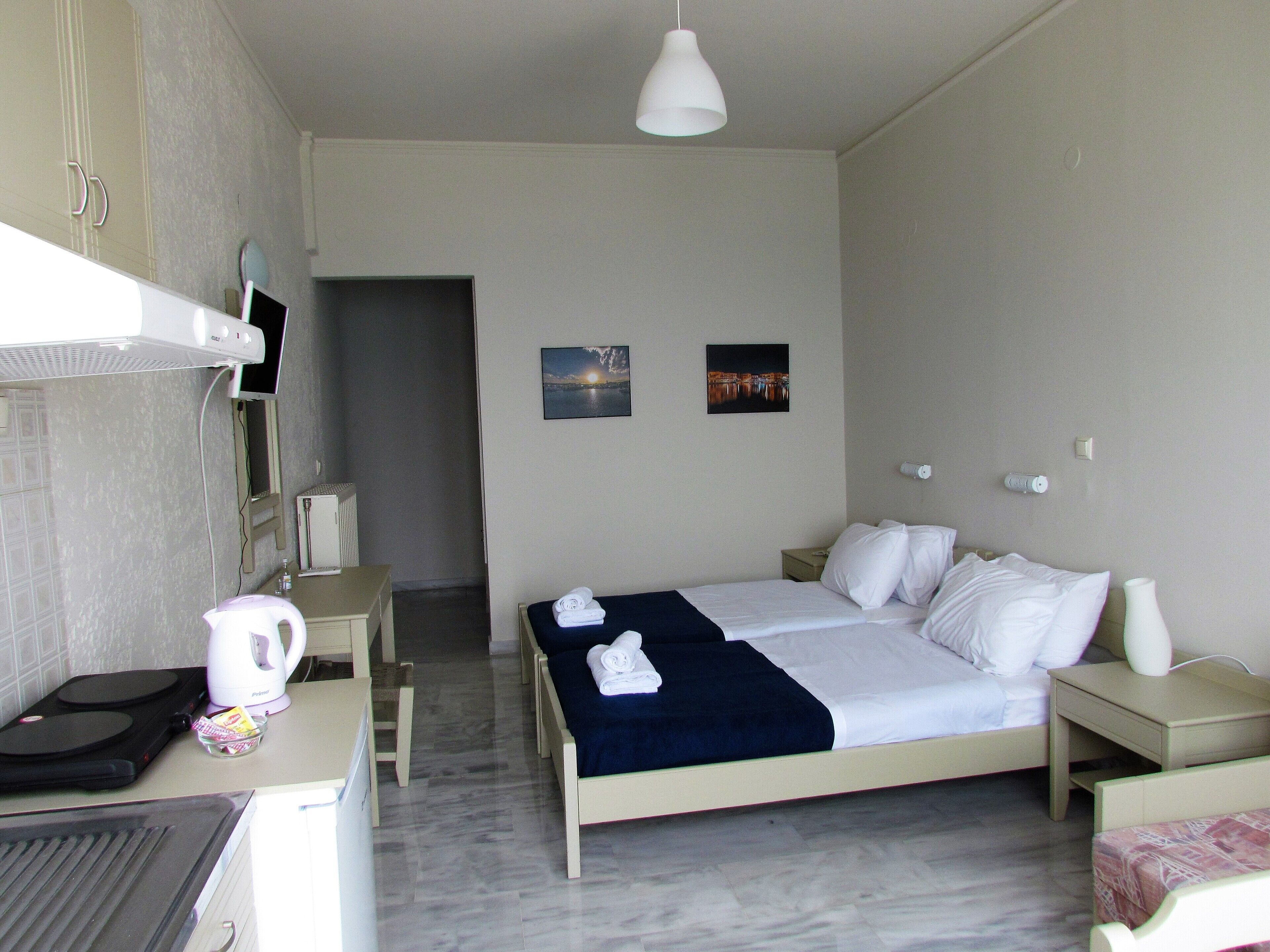 A hotel room with a bed, bedside tables, a desk with a kettle, a microwave, and a small kitchenette.