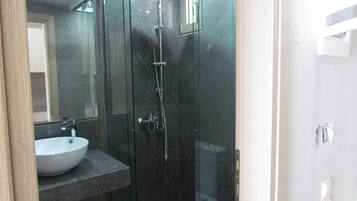 Un baño moderno con ducha de mampara de vidrio, lavamanos blanco y espejo.