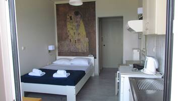 A hotel room with a bed, a desk, a kettle, and a painting on the wall.