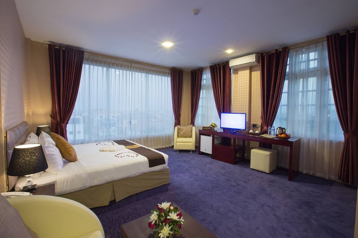 A hotel room with a bed, desk, chair, and a large window with curtains.
