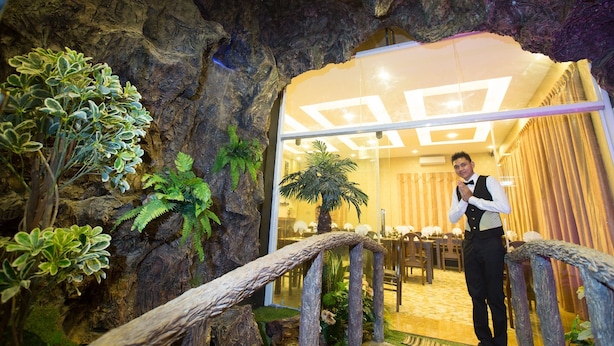 A man standing in a room with a rustic decor, including a faux rock wall and a wooden railing. - Rising Venus Hotel (Mandalay)