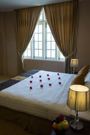 A hotel room with a bed, a bedside lamp, a fruit bowl, and curtains on a window. - Rising Venus Hotel (Mandalay)