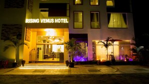 The exterior of the Rising Venus Hotel with a well-lit entrance, a visible reception area, and a landscaped outdoor area with potted plants. - Rising Venus Hotel (Mandalay)