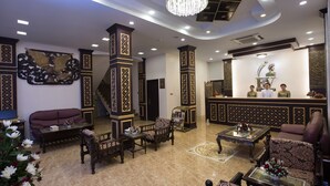 A lobby with traditional decor, including patterned columns and a reception desk with staff. - Rising Venus Hotel (Mandalay)