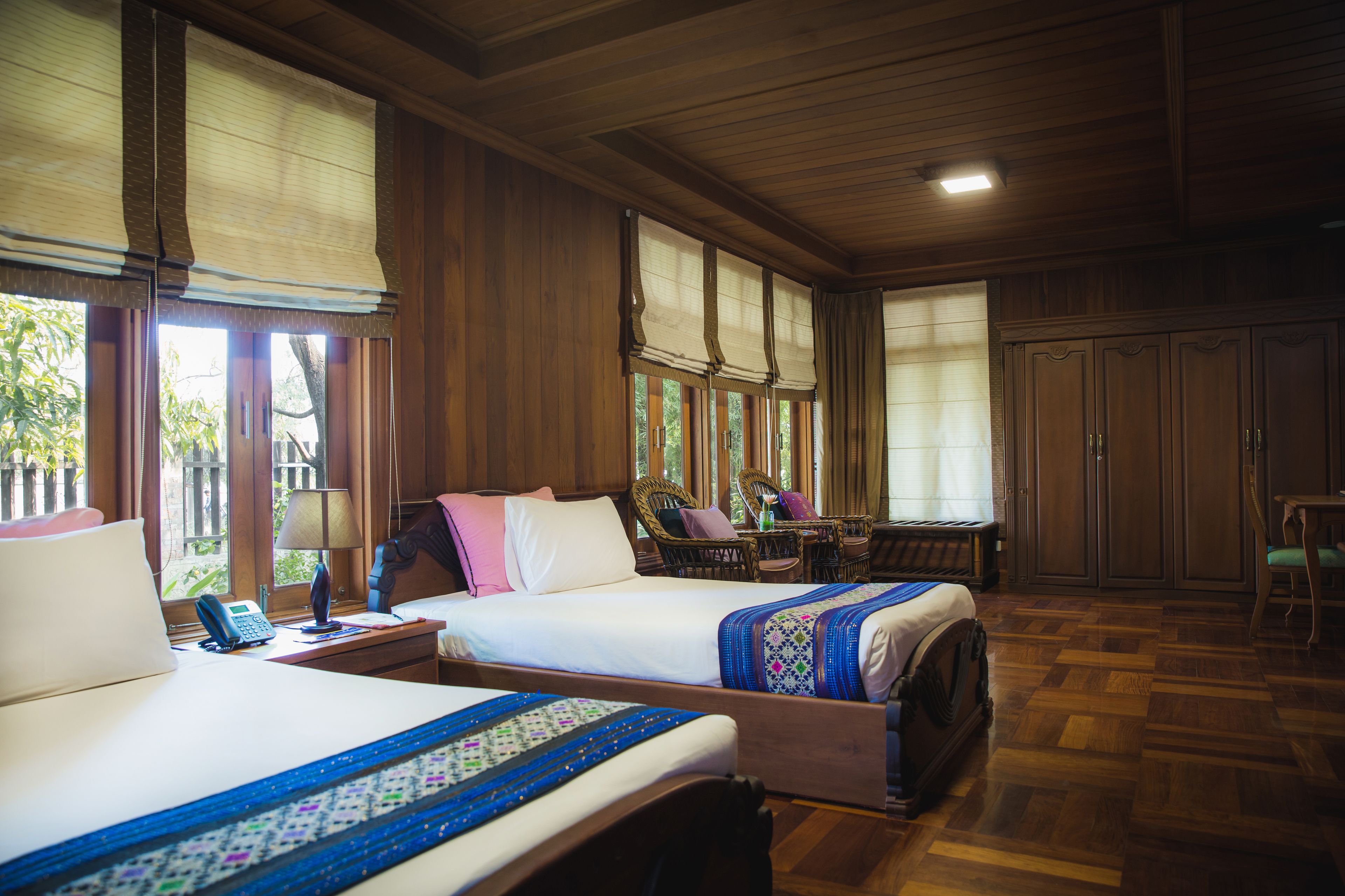 A hotel room with two beds, wooden flooring, and large windows with curtains.