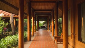 Un corredor cubierto con columnas de madera y suelo de baldosas, que conduce a un jardín.