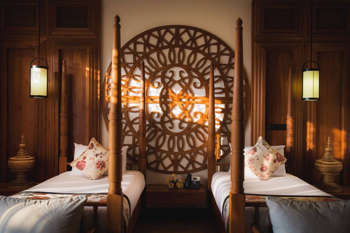 Ein Zimmer mit zwei Holzbetten, einer dekorativen Wandverkleidung und hängenden Laternen.