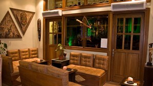 A cozy room with a sofa, armchairs, and a wooden coffee table. There is a window with a view of the street and a decorative plant on the windowsill.