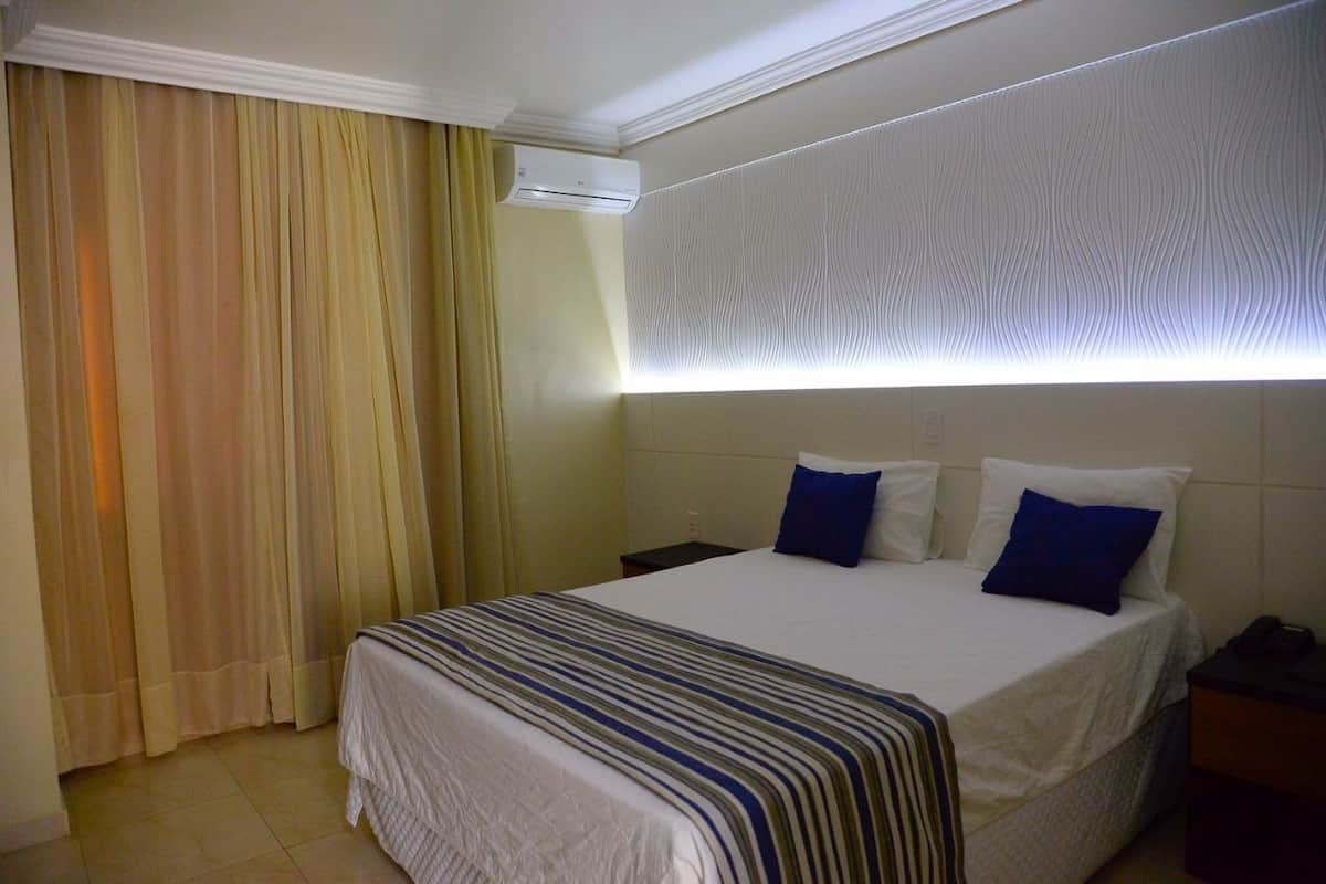 Habitació d'hotel amb llit, cortines, aire condicionat i un mur amb dibuixos.