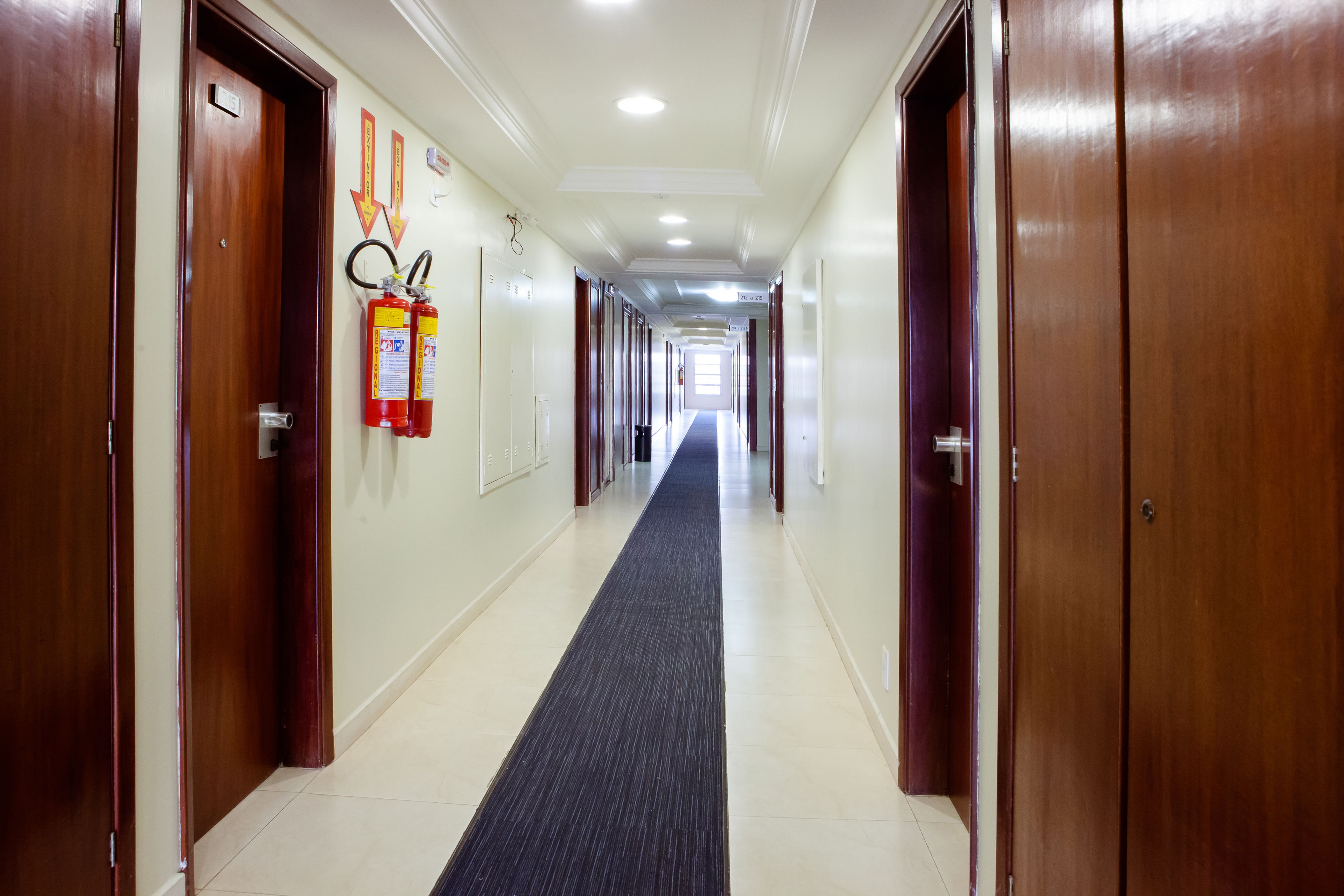 A hotel hallway with wooden doors, a black carpet, and fire extinguishers on the wall.