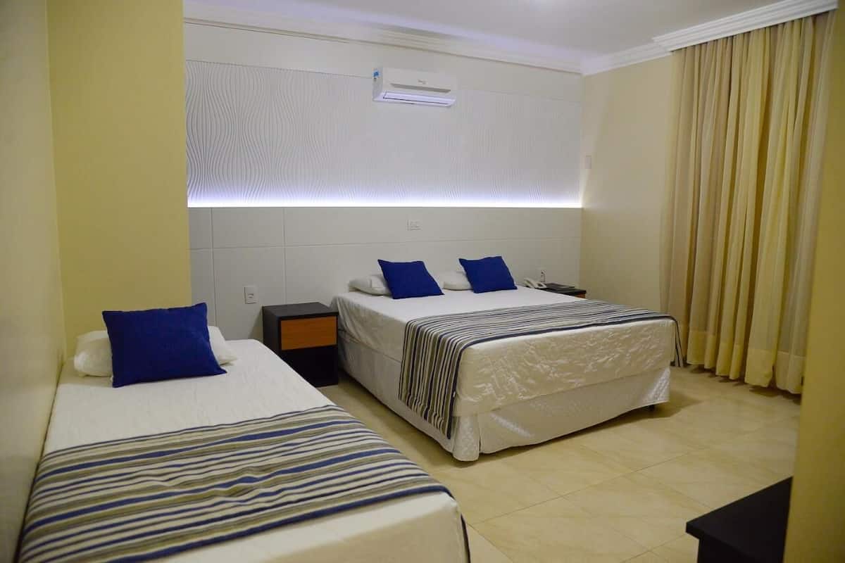 Habitació d'hotel amb dos llits individuals, una tauleta de nit i una finestra amb cortines.