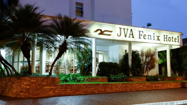 L’extérieur de l’hôtel JVA Fenix présente une entrée bien éclairée, des palmiers et un chemin en briques menant à l’entrée.