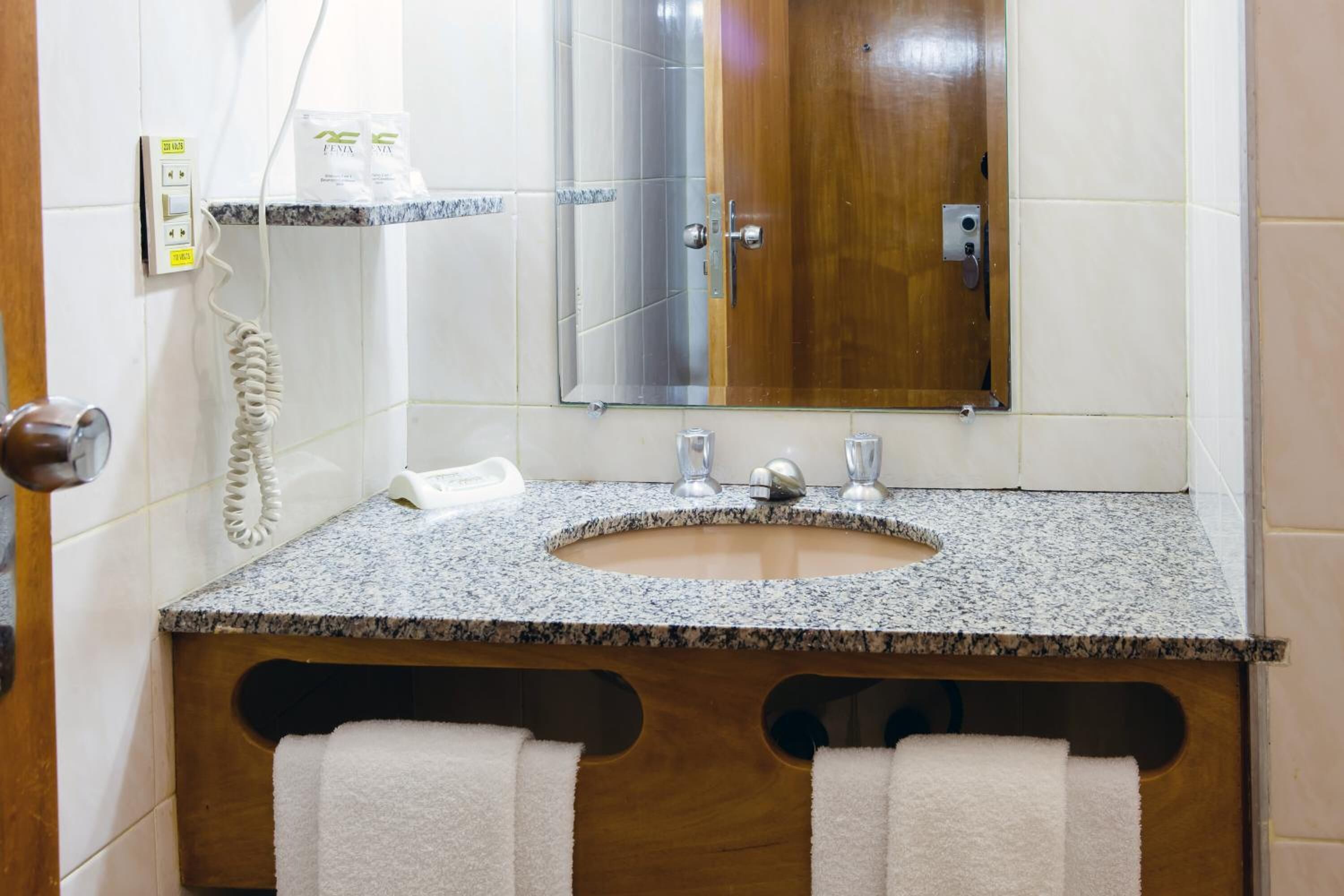 A bathroom with a granite countertop sink, a mirror, a wooden door, and a telephone.