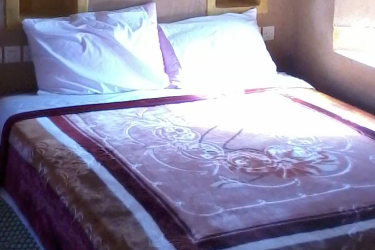 Un lit avec une couvre-lit à motifs floraux et deux oreillers, une fenêtre donnant sur un beau paysage et un mur agrémenté d’une arche décorative.