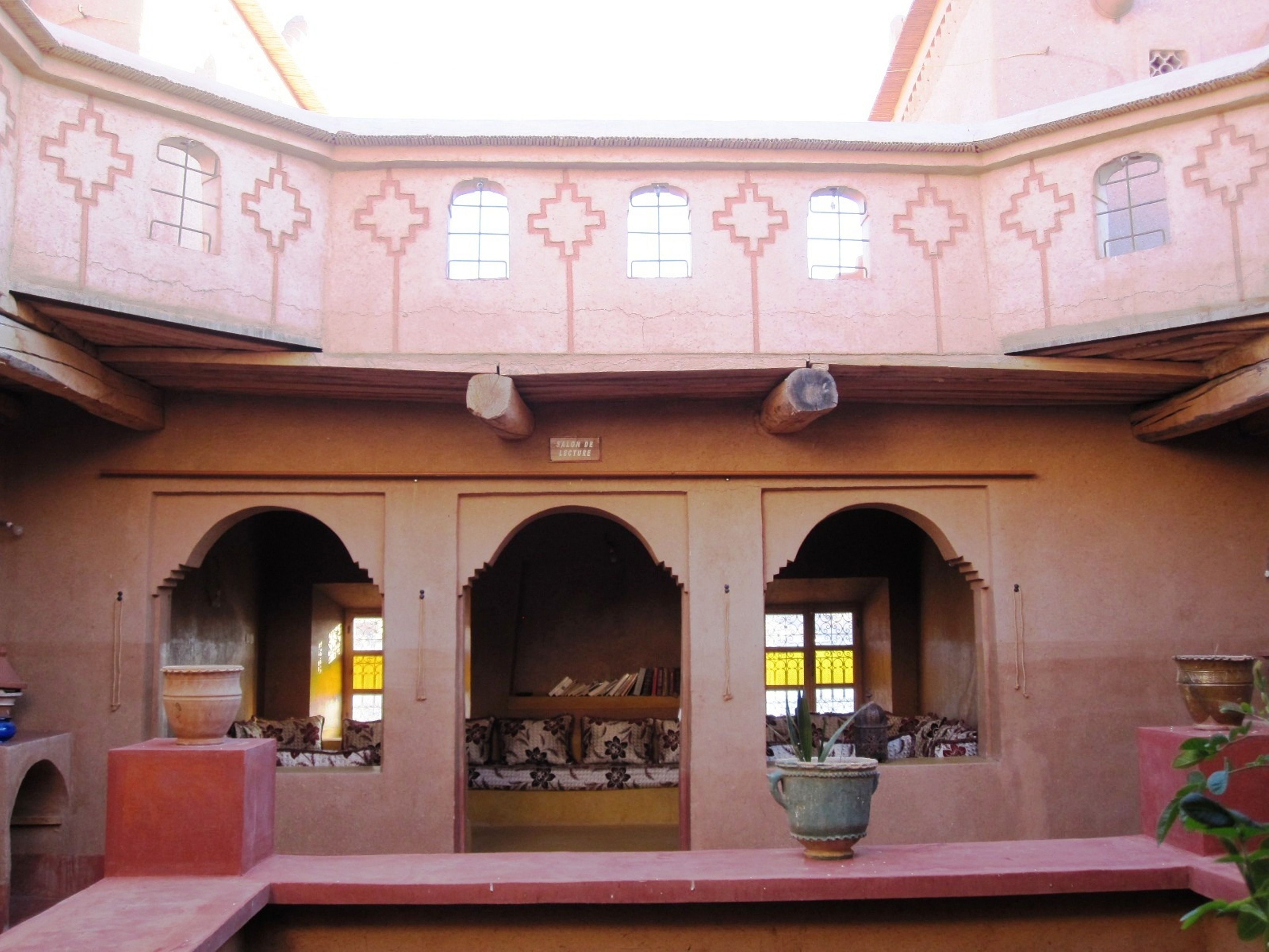 A courtyard with arches, a central seating area, and a large pot on a table.
