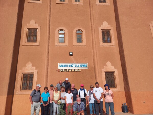 A group of people standing in front of a building with a sign that reads "CASBAH D'HÔTE LA JEANNE RECEPTION".
