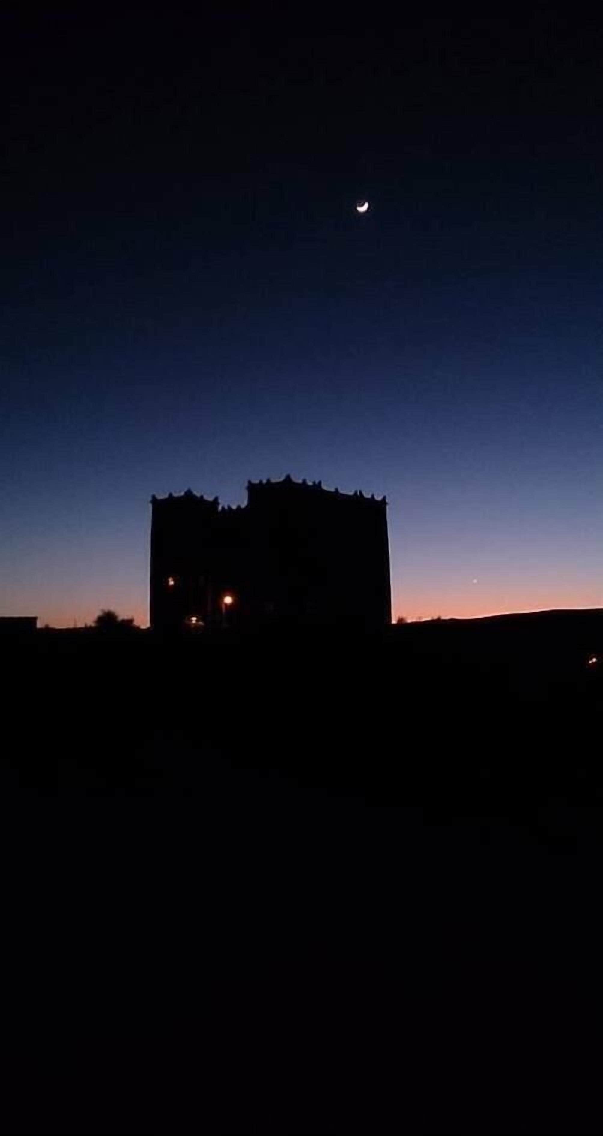 A building silhouette against a twilight sky with a crescent moon.