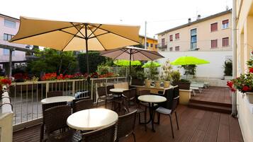 Una terrazza esterna con tavoli e sedie, grandi ombrelloni e piante in vaso.