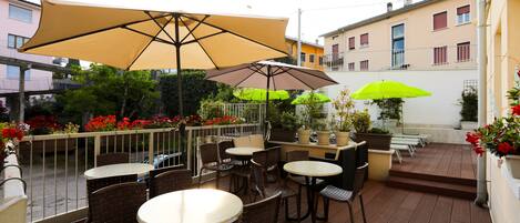 Un patio al aire libre con mesas y sillas, sombrillas grandes y plantas en macetas.