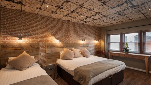 Une chambre avec deux lits, un mur en briques et un plafond orné d’un motif décoratif.
