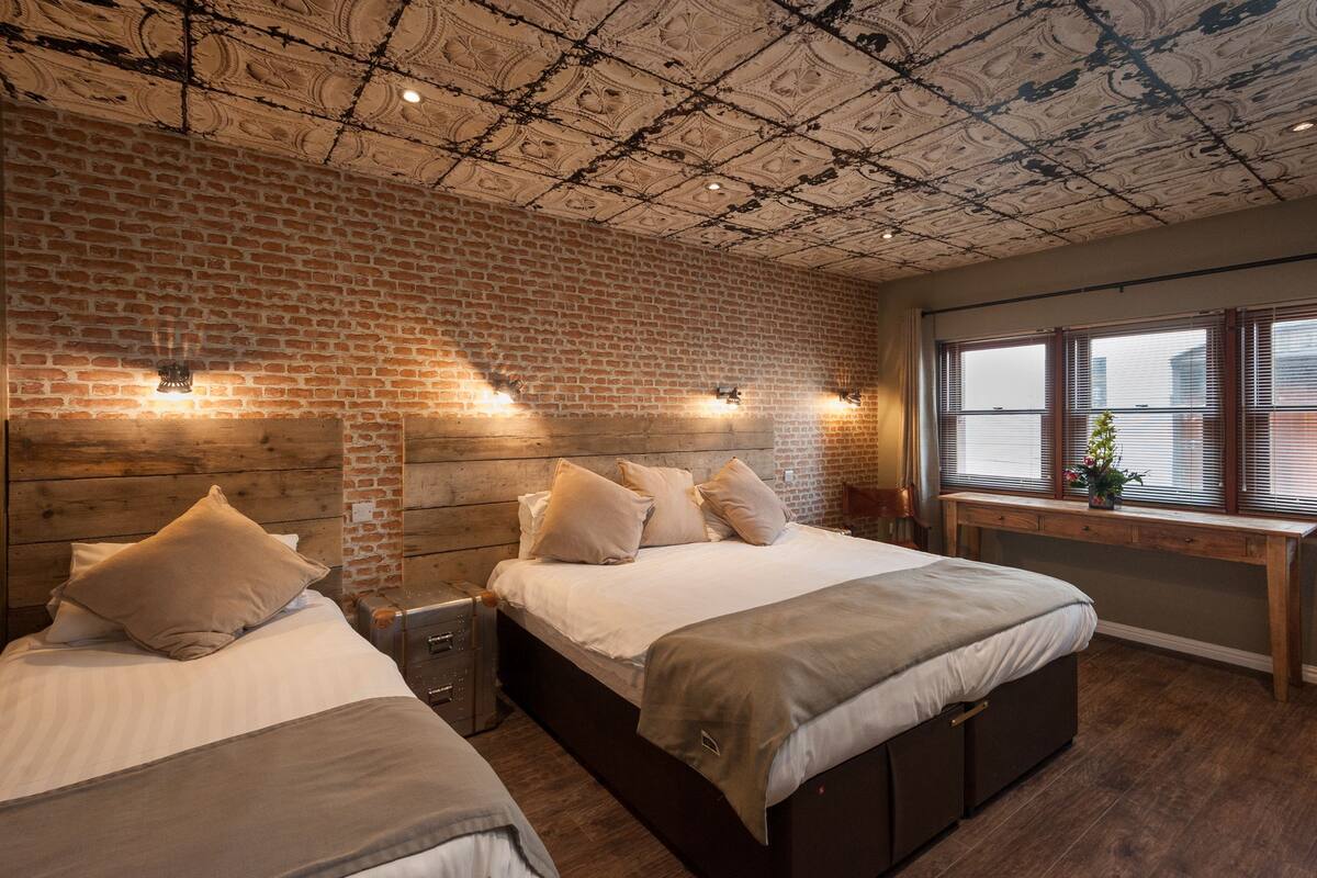 A room with two beds, a brick wall, and a ceiling with a decorative pattern.
