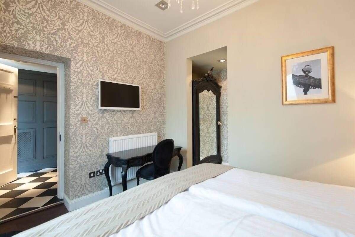 A bedroom with a bed, a desk, a chair, a television, and a framed picture on the wall.