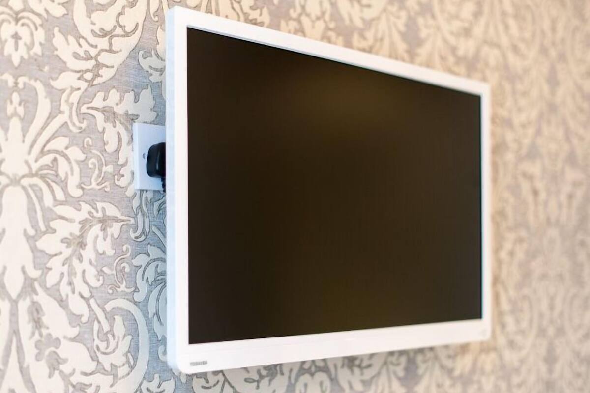 A flat-screen TV mounted on a wall with a patterned wallpaper background.