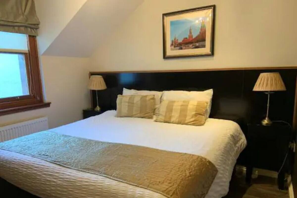 A neatly made bed with a white and beige bedspread, two bedside lamps, and a framed picture on the wall above the bed.